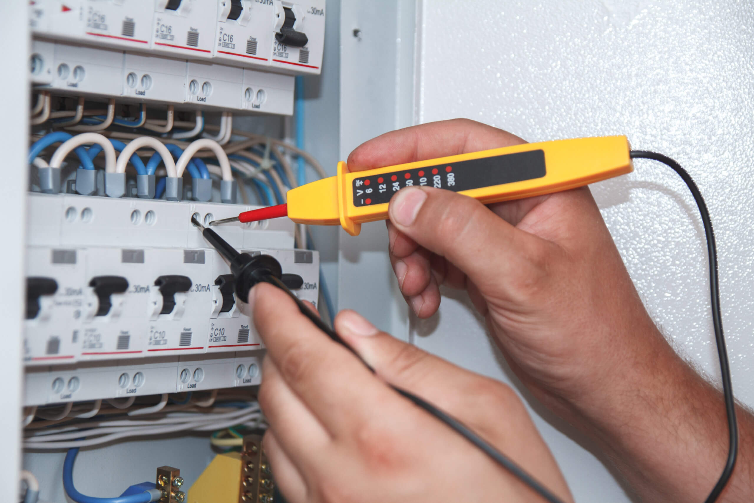 Hands of electrician with multimeter probe at an electrical switchgear cabinet examining fuse box